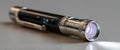 Close-up of a small black and silver flashlight emitting light on a smooth surface with shallow depth of field Royalty Free Stock Photo