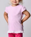 Close-up of small blonde baby girl in pink stylish t-shirt with ruffles standing holding hands at waist Royalty Free Stock Photo