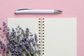 Close-up of small bouquet of fragrant blooming lavender on a blank paper notepad and white ballpoint pen over a textural pink