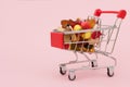 Close-up of a small cart from on a pink background, filled with multicolored sweets and marmalade.Idea - a shopaholic,a buyer,home