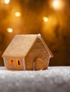 Close-up of a small gingerbread house glowing, in the snow, against a background of lights in a blur. Christmas holiday