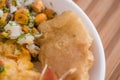 Close up of small pieces of roasted pork skin served with mashed potatoes, salad, tostado, mote inside of white bowl