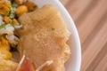 Close up of small pieces of roasted pork skin served with mashed potatoes, salad, tostado, mote inside of white bowl