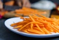 Pile of thin carrot slices on white plate with blurry background