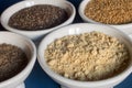 Close-up of a small plate filled with powdered golden flax seeds surrounded by small bowls of whole chia and flax seeds.