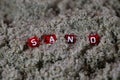 Close up of small red dices with white letters in the beachsand writing the word sand