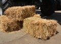 A close-up on small square haystack straw, rectangular shaped, string or wire tied bales of hay near tractor wheels