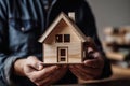 Close-Up Of A Small Wooden House Model In A Mans Hands - Generative AI