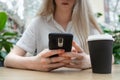 Close up of a smartphone being used by cheerful young caucasian blond business woman in a white shirt sitting at the table. Nearby Royalty Free Stock Photo