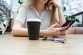 Close up of a smartphone being used by cheerful young caucasian blond business woman in a white shirt sitting at the table. Nearby Royalty Free Stock Photo