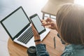 Close-up of smartphone with blank screen in hands of young woman sitting at round wooden table and touching screen