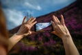 Close-up of smartphone in hands. Unknown woman using a gadget takes photos of a mountain slope covered with pink flowers. Photo