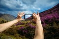 Close-up of smartphone in hands. Unknown woman using a gadget takes photos of a mountain slope covered with pink flowers