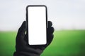 Close-up of smartphone with mockup in male hand dressed in black glove, on background of white and green background.