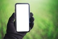 Close-up of smartphone with mockup in male hand dressed in black glove, on blurred green background. Royalty Free Stock Photo