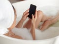 Close up of smartphone screen in female hands in bathtub. Over shoulder view of naked woman typing on smartphone in tub