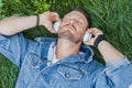 Close up of man lying on green grass and listening to music on headphones. Royalty Free Stock Photo