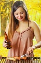 Close up of smiling beautiful young woman holding a bottle in one hand and using a tongs and turning the grilling Royalty Free Stock Photo