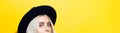 Close-up of smiling blue eyes of young blonde girl wearing black round hat, panoramic portrait on yellow background. Royalty Free Stock Photo