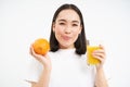 Close up of smiling brunette girl, drinks fresh juice, holds orange fruit, white studio background Royalty Free Stock Photo