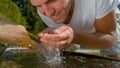 CLOSE UP: Smiling Caucasian man lifts up a handful of glassy water to drink.