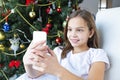 Close up smiling caucasian young preteen girl talking on phone, sitting near festive Christmas tree at home, happy Royalty Free Stock Photo