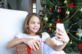 Close up smiling caucasian young preteen girl talking on phone, sitting near festive Christmas tree at home, happy Royalty Free Stock Photo