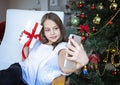 Close up smiling caucasian young preteen girl talking on phone, sitting near festive Christmas tree at home, happy Royalty Free Stock Photo