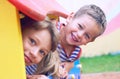 Close up of smiling childs face hiding behind wooden element of slide at playground on summer day. Royalty Free Stock Photo