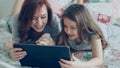 Close-up of smiling cute girl and young mother in pajamas laughing and looking in digital tablet while lying on bed at Royalty Free Stock Photo