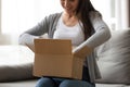 Happy young woman unboxing cardboard parcel at home.