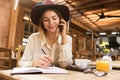 Close up of a smiling girl in hat sitting at the cafe table indoors, talking on mobile phone Royalty Free Stock Photo