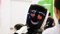 Close-up of smiling and happy male robot`s face looking at the visitors of large exhibition. Media. Different working