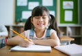 Close-up smiling junior Asian student girl sits at desk in class and writing in notebook. Portrait of happy Asia school girl smile Royalty Free Stock Photo