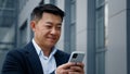 Close up smiling laughing Asian middle-aged Korean businessman man employer entrepreneur laugh looking at mobile phone Royalty Free Stock Photo