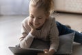 Close up smiling little girl using tablet, lying on floor Royalty Free Stock Photo