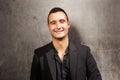 Close up smiling man posing against gray wall with black blazer