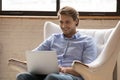 Close up smiling man using laptop, sitting in cozy armchair Royalty Free Stock Photo