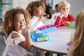 Close up of smiling young children sitting at a table eating their packed lunches together at infant school, girl smiling to camer