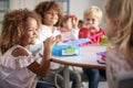 Close up of smiling young children sitting at a table eating their packed lunches together at infant school, selective focus