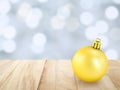 shiny yellow gold christmas ball on vintage brown wooden desk top with defocused pastel blue and white of snow and lights bokeh