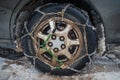 Close-up of snow chains mounted on a snow-covered and dirty car wheel. The concept of safety on snowy roads.