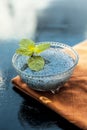 Close up of soaked sabja seeds or falooda seeds or sweet basil seeds in a glass bowl on brown colored napkin on wooden surface wit