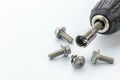 Close-up of a socket wrench attached to a drill surrounded by shiny steel bolts on a white surface Royalty Free Stock Photo