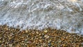 Close up soft wave lapped the gravel beach. Beautiful sea waves with foam. Abstract texture background