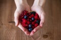 Some hands holding blueberries and raspberries over wooden background.