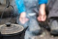 Close-up of a sooty teapot with a lid hanging and basking over a campfire, on a blurry background.