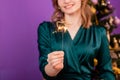 Close-up of a sparkler in the hands of a young woman in a green dress standing against the background of a Christmas tree Royalty Free Stock Photo