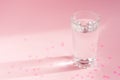 Close up of sparkling water in transparent glass and sun glare on pink background wth scattered pape hearts Royalty Free Stock Photo