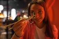 Close-up of spicy asparagus in sticks. Smiling young woman eating vegetarian Asian dish with chopsticks. Red light. Royalty Free Stock Photo